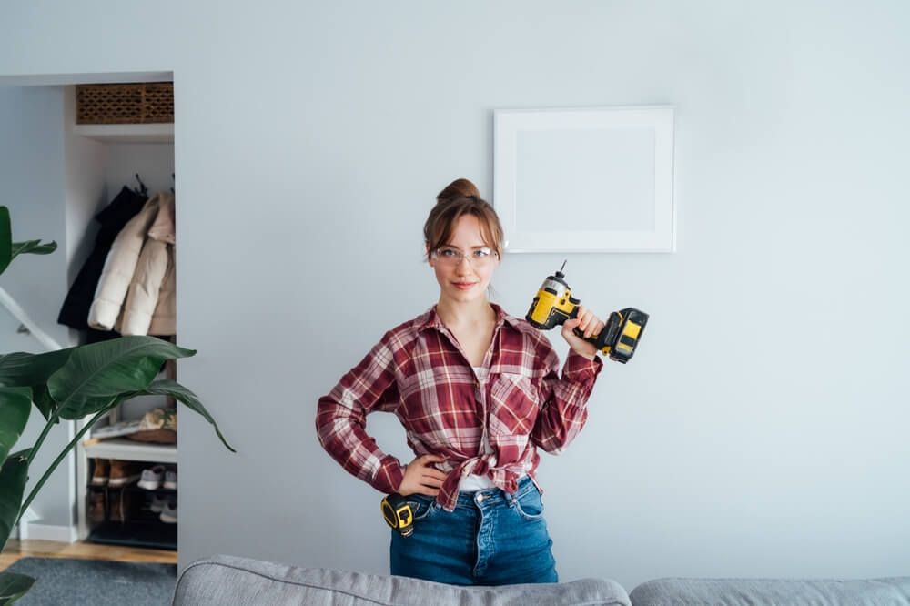 A girl holding in her hand a drilling machine and wear a safety glasses
